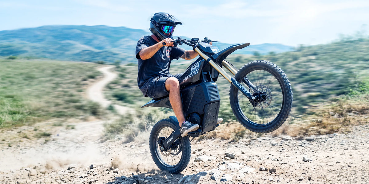 Rider performing a wheelie on a Nexvey Storm electric dirt bike on an off-road mountain trail.