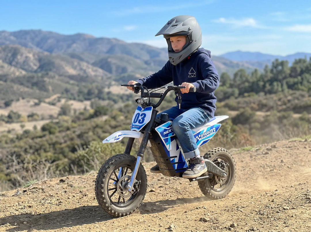 Young boy wearing a full-face helmet riding a Nexvey Spark 03 electric dirt bike on an off-road mountain trail