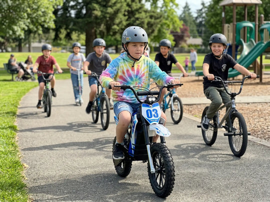 A group of kids riding bikes and scooters in a park, featuring a boy leading on a Nexvey Spark 03 electric dirt bike