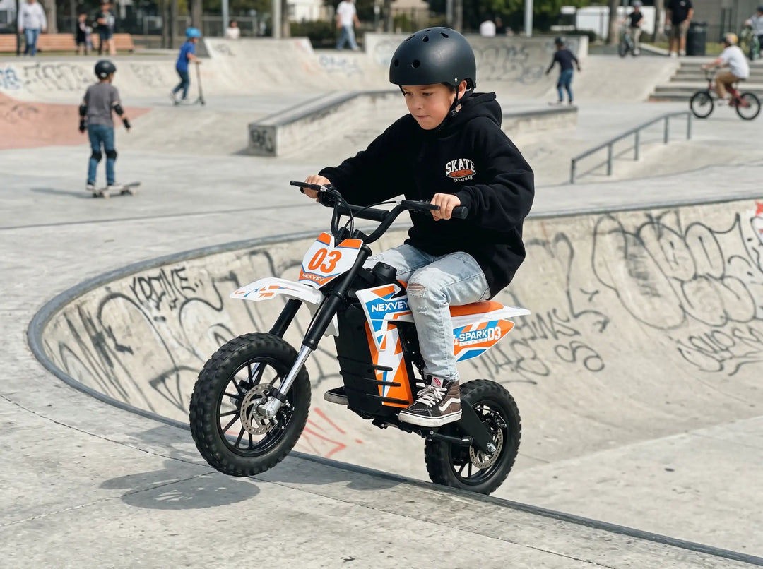 A young boy wearing a helmet and hoodie riding an orange and white NEXVEY SPARK 03 electric dirt bike on concrete bowls and ramps at a concrete skatepark