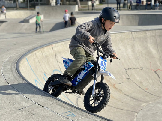Young boy riding a Nexvey Spark 03 electric dirt bike on a concrete ramp at a skate park